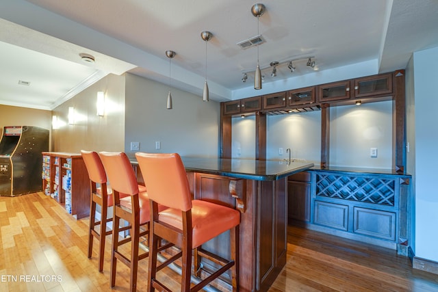 bar featuring rail lighting, ornamental molding, dark wood-type flooring, and hanging light fixtures