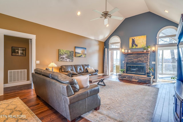 living room featuring ceiling fan, a stone fireplace, dark wood-type flooring, and high vaulted ceiling