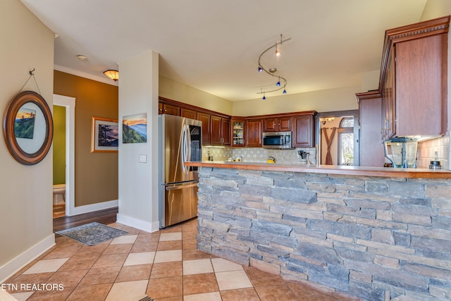 kitchen with stainless steel appliances, backsplash, kitchen peninsula, light tile patterned floors, and ornamental molding