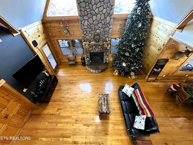 living room featuring hardwood / wood-style flooring, wood walls, a stone fireplace, and a towering ceiling