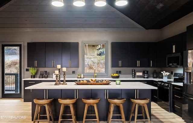 kitchen featuring light hardwood / wood-style floors, a kitchen island, a breakfast bar area, and black appliances