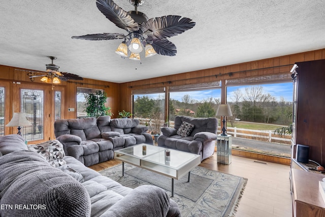 living area featuring a ceiling fan, light wood-type flooring, visible vents, and wooden walls