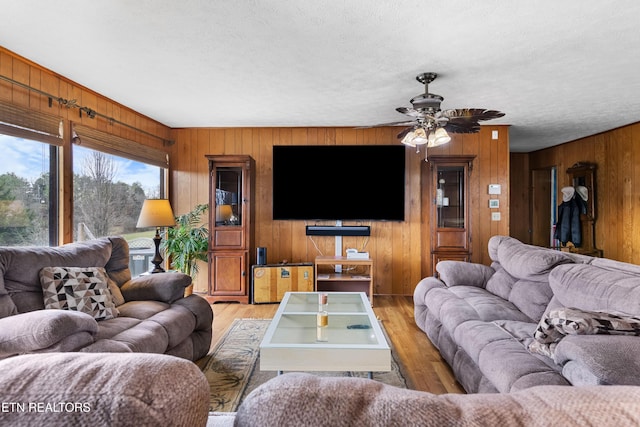 living area with ceiling fan, wood walls, a textured ceiling, and wood finished floors