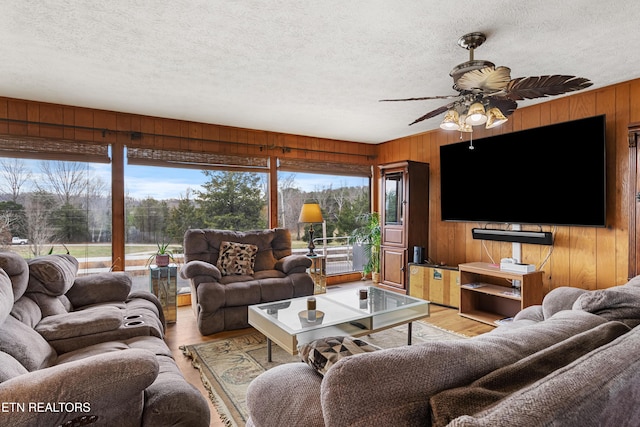 living room with a textured ceiling, ceiling fan, wood walls, and light wood-style floors