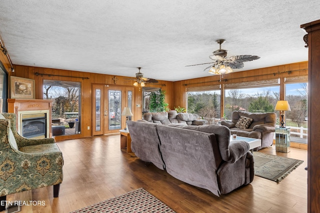 living area with a textured ceiling, a glass covered fireplace, wood finished floors, and wooden walls