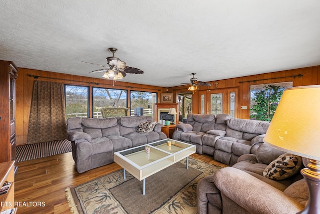 living room featuring a fireplace, dark wood finished floors, a ceiling fan, wooden walls, and a textured ceiling