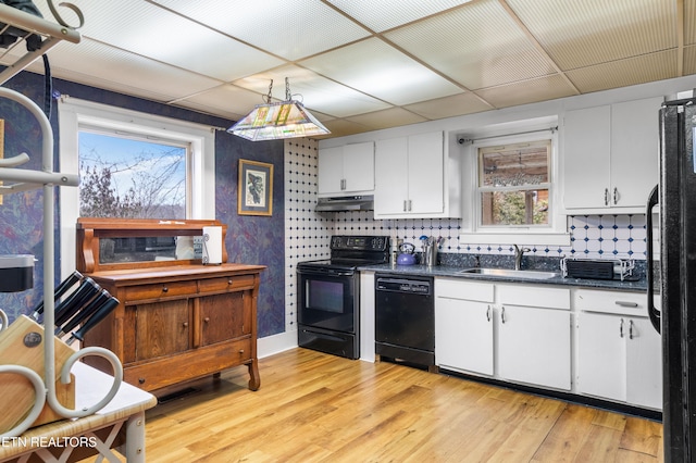 kitchen featuring white cabinets, light wood-style flooring, under cabinet range hood, black appliances, and a sink