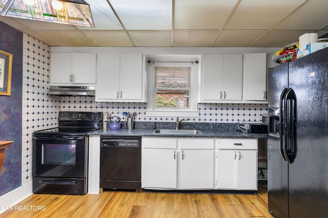 kitchen with a drop ceiling, under cabinet range hood, black appliances, white cabinetry, and a sink