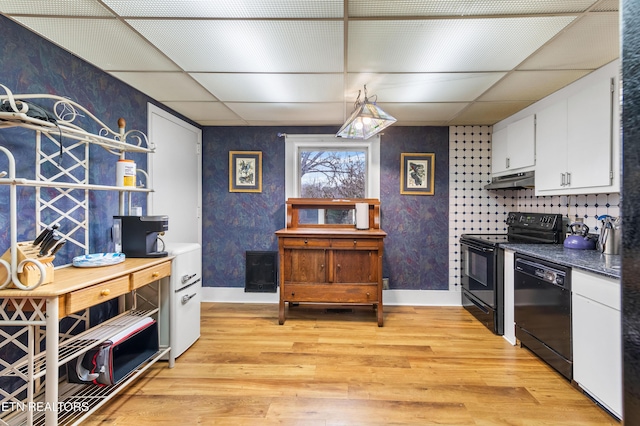 kitchen with black appliances, light wood-style floors, a drop ceiling, and white cabinets