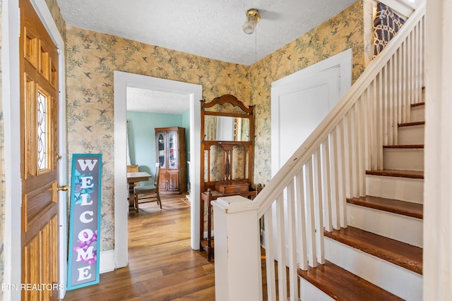 entrance foyer featuring stairs, wood finished floors, a textured ceiling, and wallpapered walls