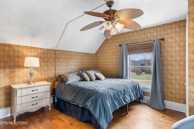 bedroom with lofted ceiling, wallpapered walls, a textured ceiling, and wood finished floors