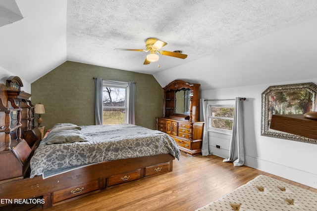 bedroom with lofted ceiling, multiple windows, light wood-type flooring, and a textured ceiling