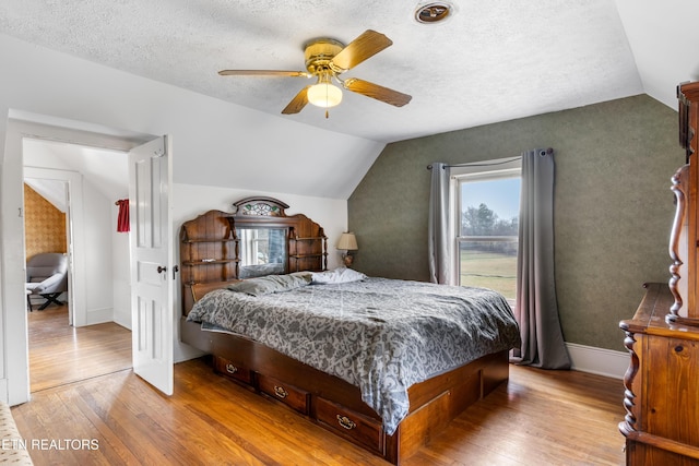 bedroom featuring lofted ceiling, light wood finished floors, a textured ceiling, and baseboards