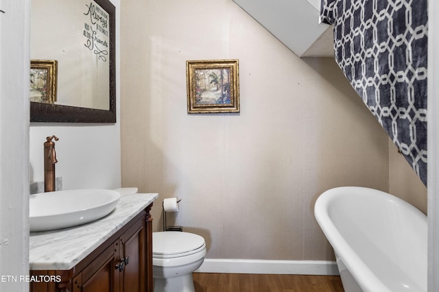 full bathroom featuring toilet, vanity, wood finished floors, a freestanding tub, and baseboards