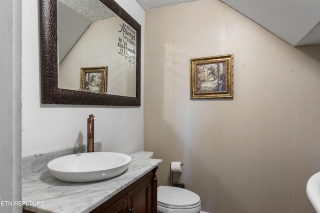 half bath with toilet, vaulted ceiling, and vanity