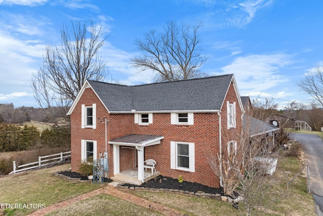 view of front of home featuring a front yard, brick siding, fence, and roof with shingles