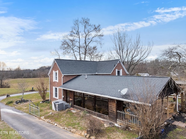 exterior space featuring a shingled roof, central AC unit, and brick siding