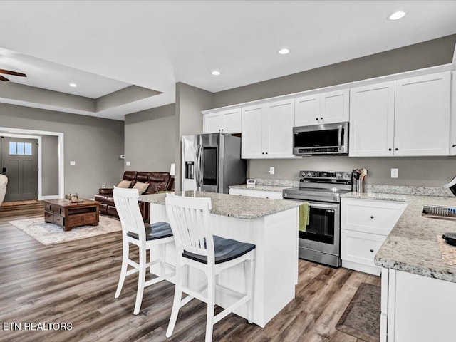 kitchen with light stone countertops, appliances with stainless steel finishes, a kitchen island, dark hardwood / wood-style flooring, and white cabinetry