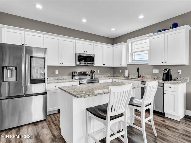 kitchen featuring white cabinets, dark hardwood / wood-style floors, appliances with stainless steel finishes, a kitchen island, and light stone counters