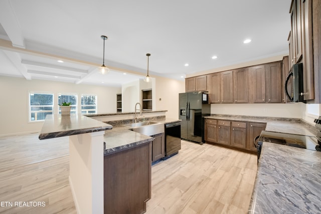 kitchen featuring sink, hanging light fixtures, an island with sink, beam ceiling, and black appliances