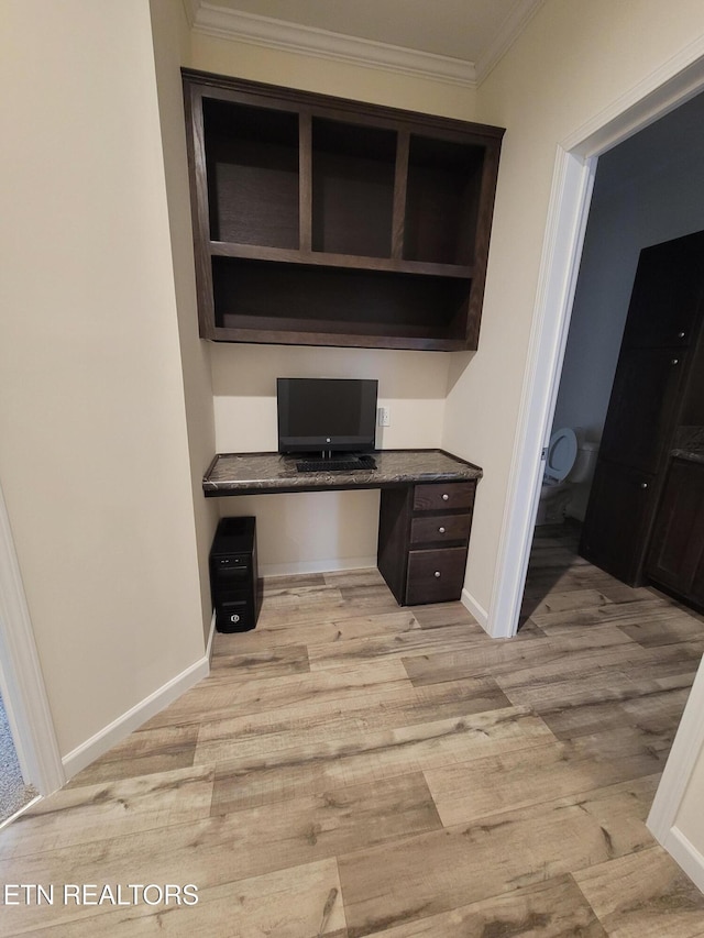 unfurnished office featuring ornamental molding, built in desk, and light hardwood / wood-style flooring