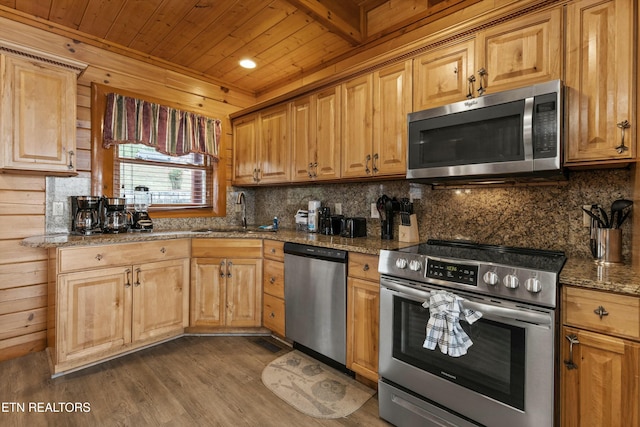 kitchen featuring appliances with stainless steel finishes, dark hardwood / wood-style flooring, wooden walls, sink, and stone countertops