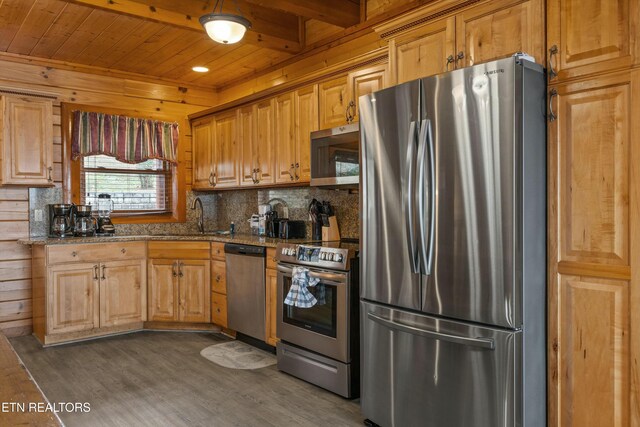 kitchen with light stone countertops, stainless steel appliances, sink, dark hardwood / wood-style floors, and wood walls