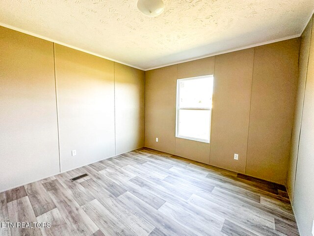 empty room featuring a textured ceiling, light wood-type flooring, and crown molding