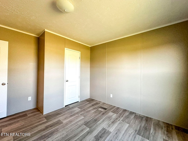 unfurnished bedroom with a textured ceiling, hardwood / wood-style flooring, and ornamental molding