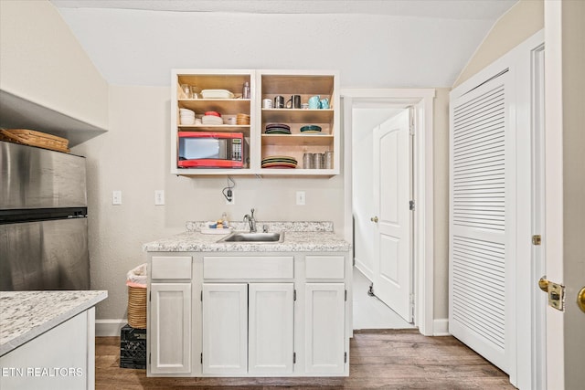 kitchen featuring lofted ceiling, sink, light wood-type flooring, appliances with stainless steel finishes, and white cabinetry