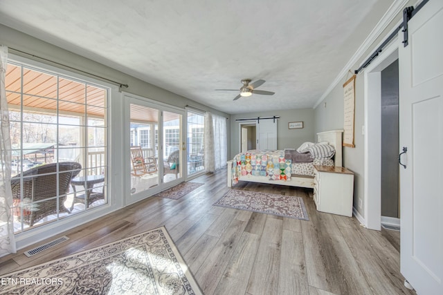 bedroom featuring a barn door, light hardwood / wood-style flooring, and ornamental molding