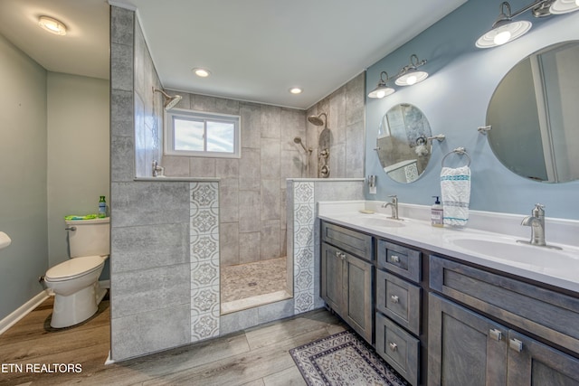 bathroom featuring hardwood / wood-style flooring, vanity, toilet, and a tile shower