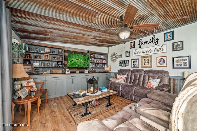 living room featuring ceiling fan, built in shelves, and light hardwood / wood-style flooring