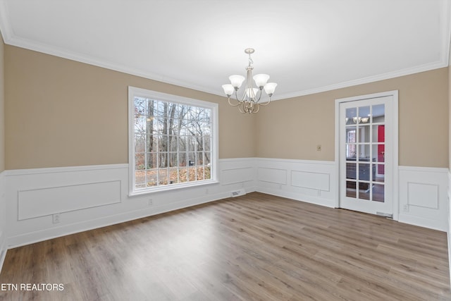 unfurnished dining area with hardwood / wood-style flooring, crown molding, and an inviting chandelier