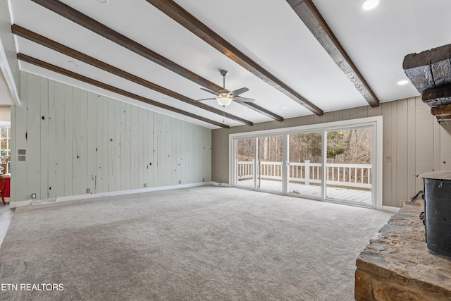 unfurnished living room featuring beamed ceiling, ceiling fan, wooden walls, and carpet