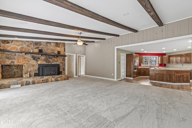 unfurnished living room with wooden walls, hardwood / wood-style flooring, ceiling fan, a fireplace, and beamed ceiling