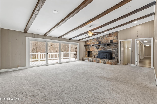 unfurnished living room featuring beamed ceiling, ceiling fan, a fireplace, and carpet