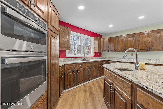 kitchen featuring double oven, light stone countertops, light hardwood / wood-style flooring, and sink