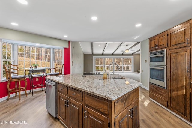 kitchen featuring a healthy amount of sunlight, a kitchen island with sink, appliances with stainless steel finishes, and light hardwood / wood-style flooring