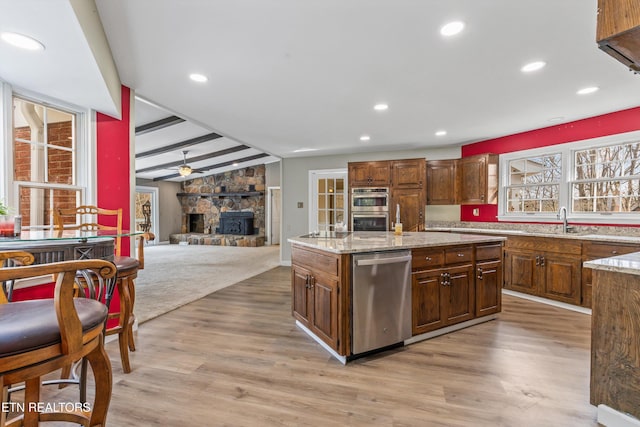 kitchen with a stone fireplace, ceiling fan, light stone countertops, light wood-type flooring, and stainless steel appliances