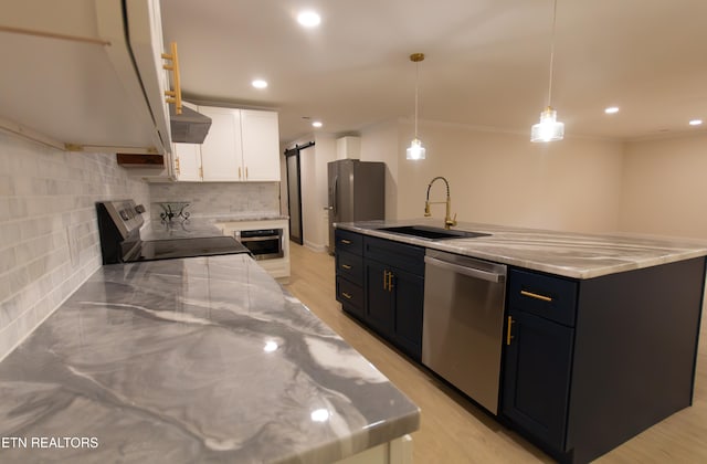 kitchen featuring pendant lighting, sink, a barn door, appliances with stainless steel finishes, and white cabinetry