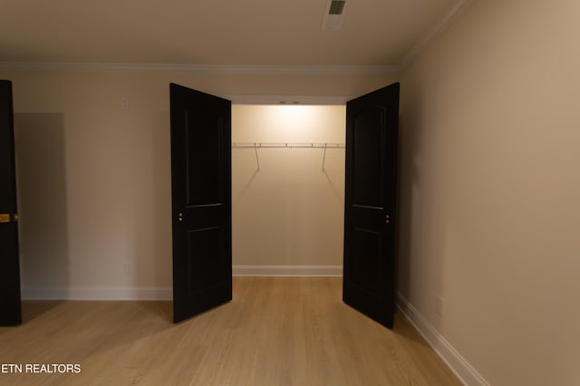 unfurnished bedroom featuring crown molding, a closet, and light wood-type flooring