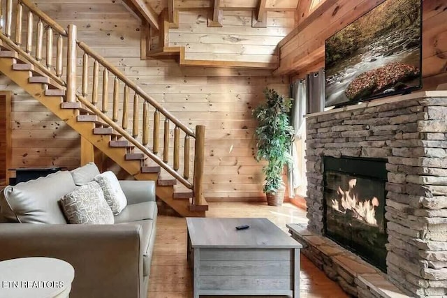 unfurnished living room with beamed ceiling, hardwood / wood-style flooring, a stone fireplace, and wooden walls