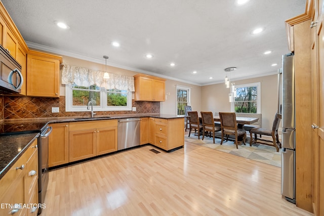 kitchen with sink, hanging light fixtures, stainless steel appliances, ornamental molding, and light wood-type flooring