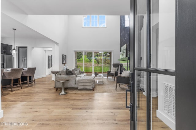 living room with a towering ceiling, light hardwood / wood-style floors, and plenty of natural light