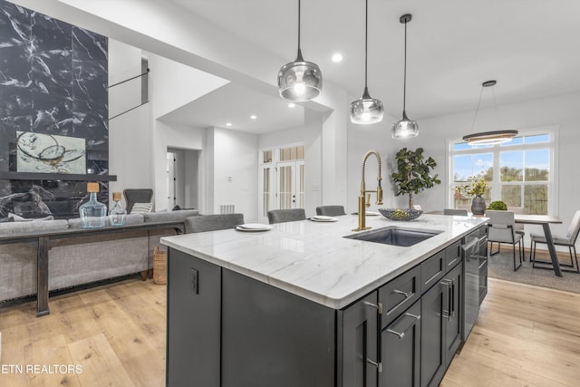 kitchen featuring light hardwood / wood-style floors, sink, light stone countertops, and an island with sink