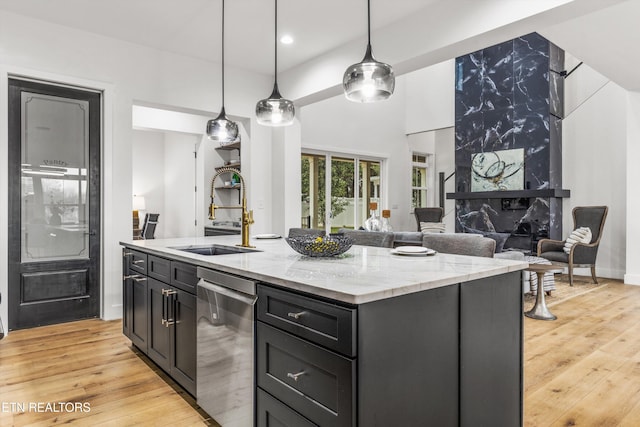 kitchen featuring a kitchen island with sink, sink, light stone countertops, light wood-type flooring, and decorative light fixtures