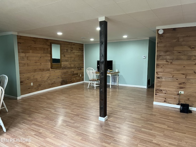 basement featuring light hardwood / wood-style floors, ornamental molding, and wood walls