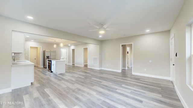 unfurnished living room featuring ceiling fan, sink, and light wood-type flooring