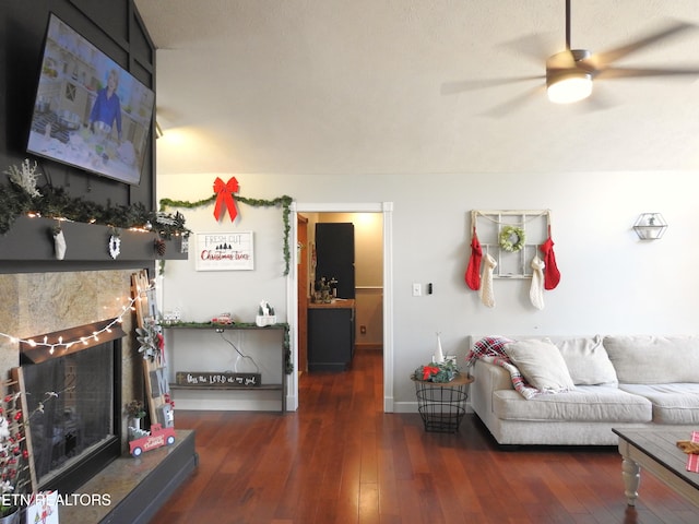 living room with a fireplace, ceiling fan, and dark wood-type flooring